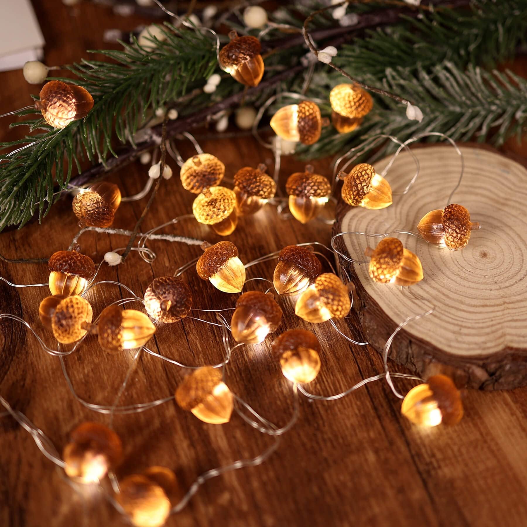 String lights shaped like acorns with warm LED lights, arranged on a wooden surface with pine branches.