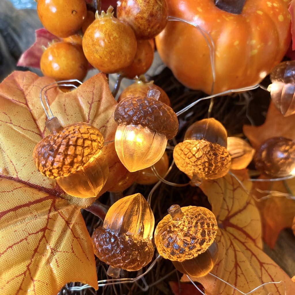 Close-up of acorn-shaped string lights with warm LED glow, surrounded by fall leaves and decorative pumpkins.