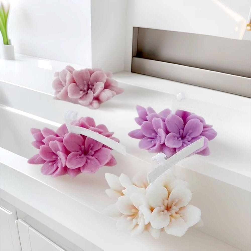Four floral-shaped silicone molds in pink, purple, and white on a white shelf.