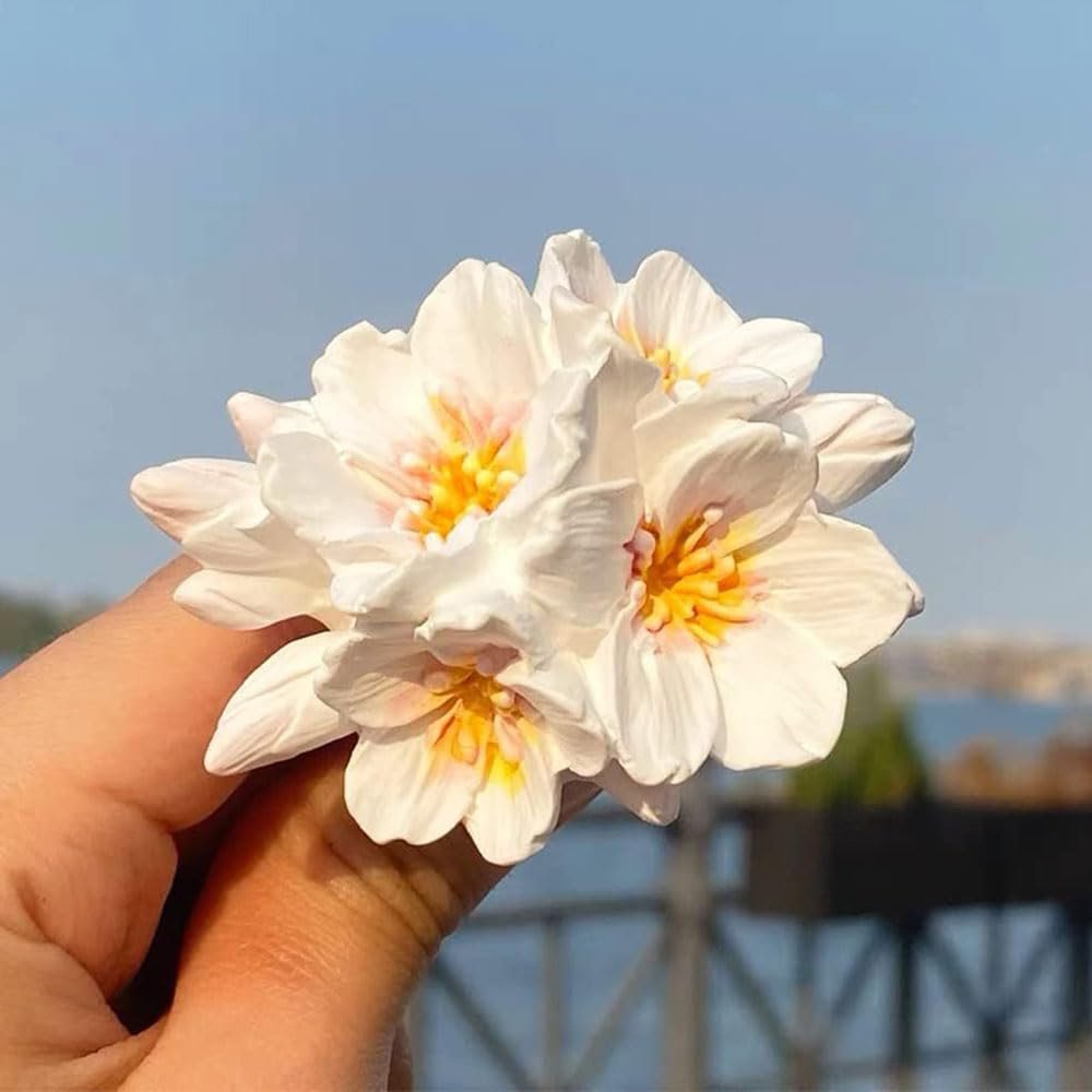 Hand holding a white cherry blossom flower mold with yellow and pink accents against a blue sky.