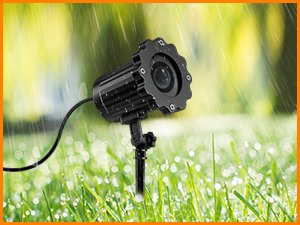Outdoor Halloween projector light with adjustable head sitting in wet grass with rain falling
