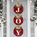 Three round buffalo plaid Christmas wreath signs spelling JOY, hanging on a door with festive decorations.