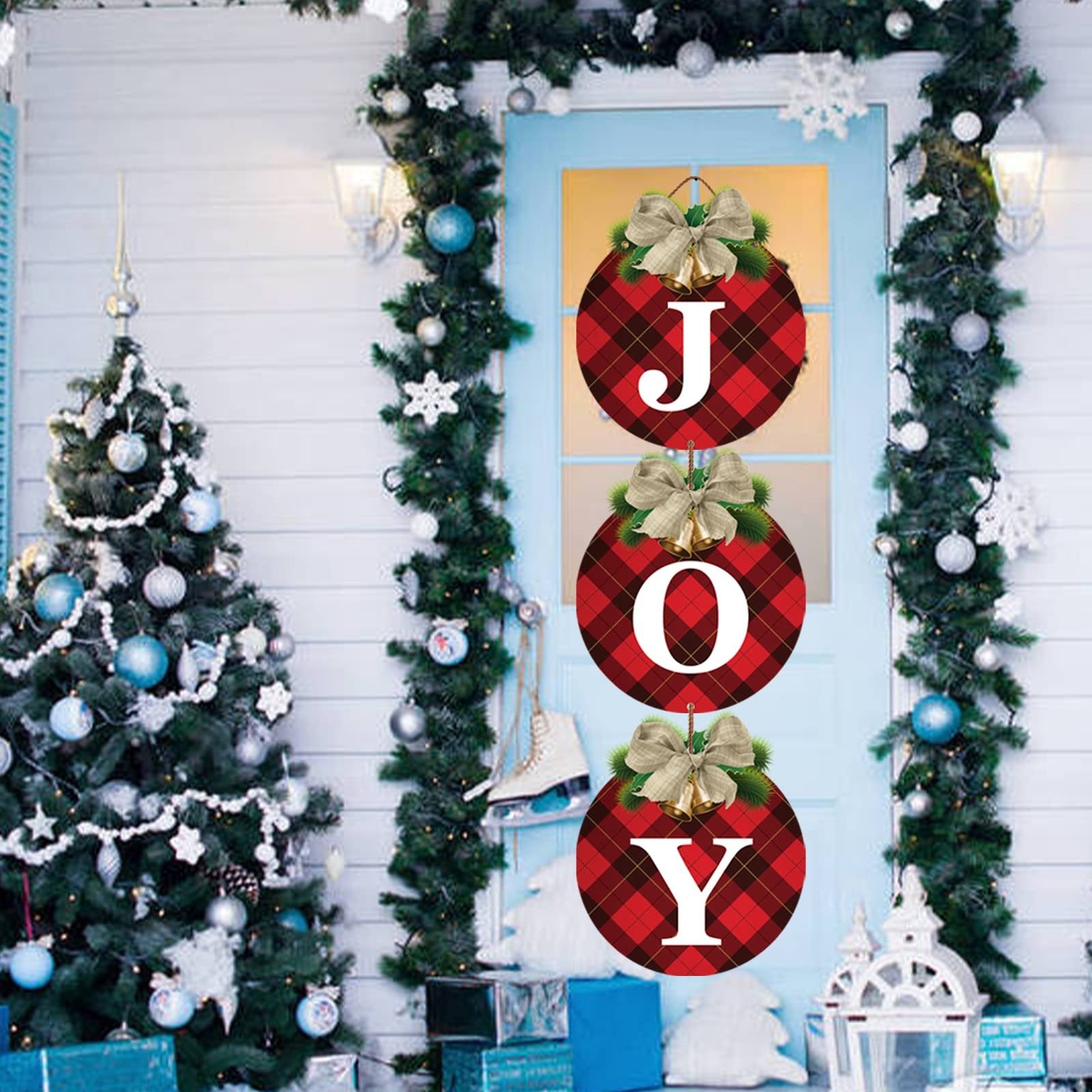 Three round buffalo plaid Christmas ornaments spelling JOY hanging on a blue door, decorated with garland and a Christmas tree.