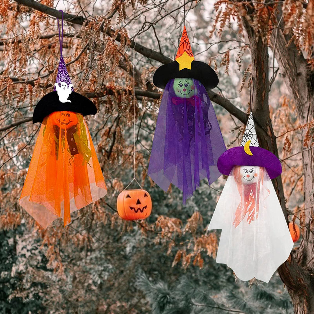 Three Halloween hanging ghost decorations with witch hats and pumpkin faces, suspended from tree branches.