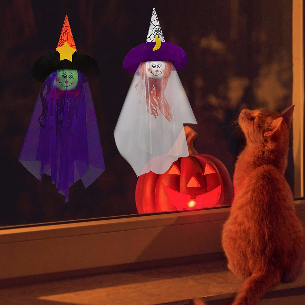 Two Halloween hanging ghost decorations and a lit pumpkin with a cat looking up at them through a window