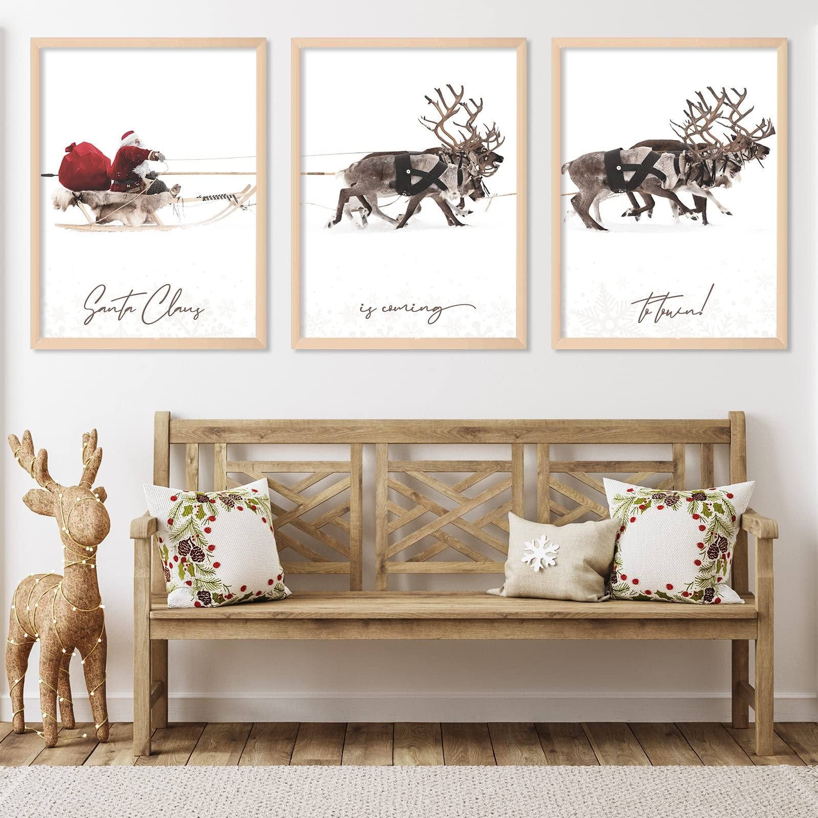 Three framed Christmas art prints depicting Santa Claus in a sleigh and reindeer pulling a sleigh, displayed above a wooden bench with festive pillows.
