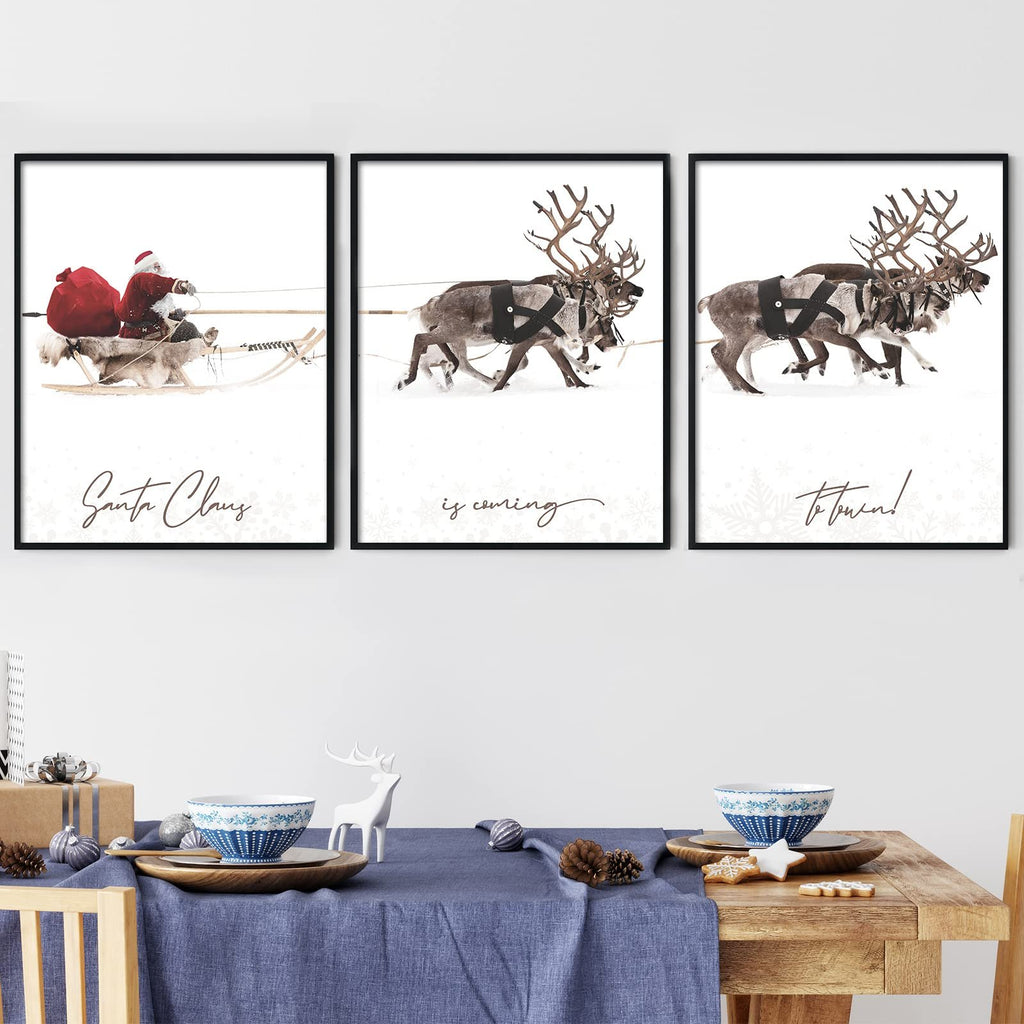 Three framed Christmas wall art prints depicting Santa Claus in a sleigh and reindeer in the snow, displayed above a decorated table.