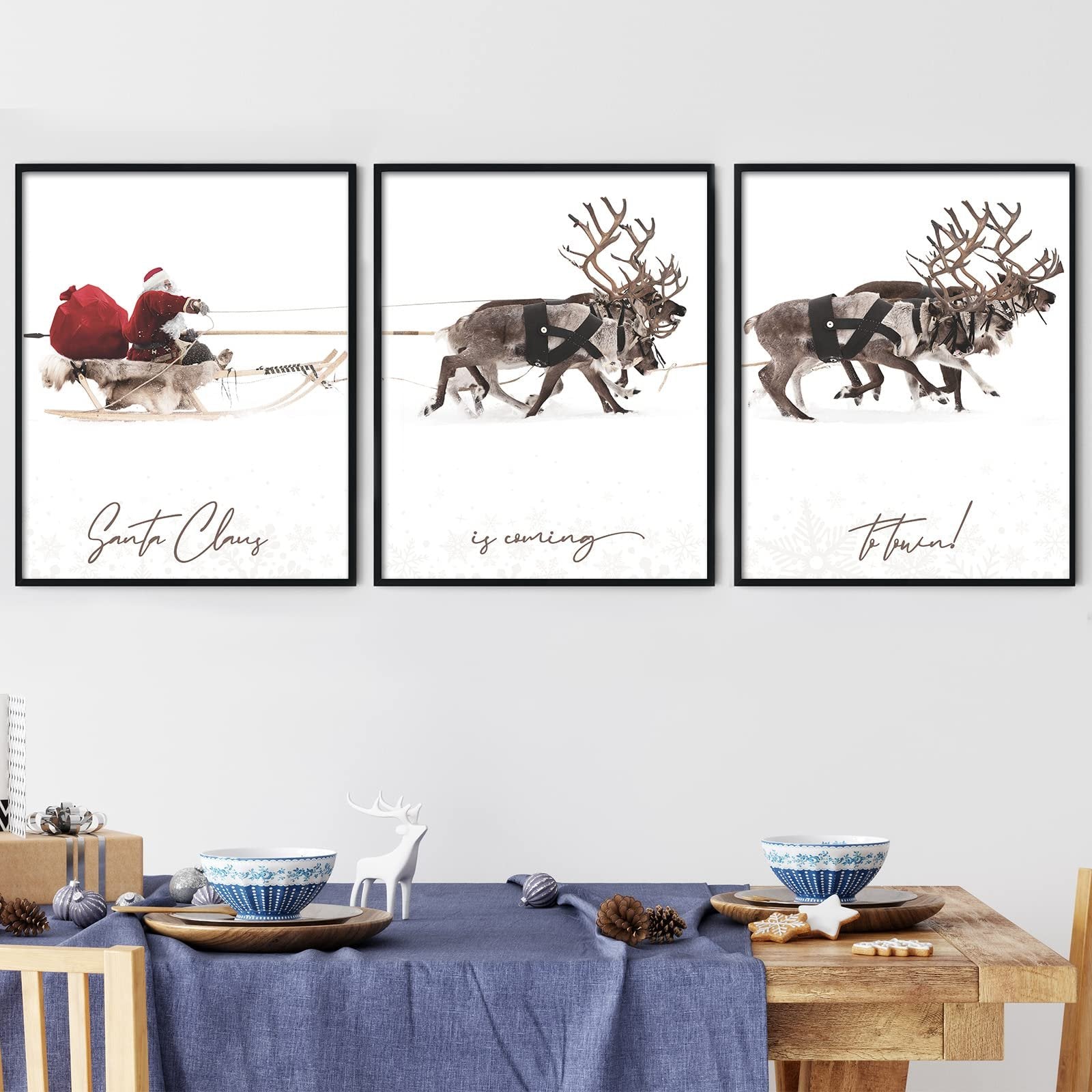 Three framed Christmas wall art prints depicting Santa Claus in a sleigh and reindeer in the snow, displayed above a decorated table.