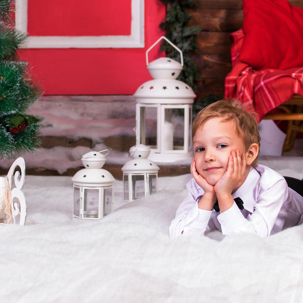 Young boy in a white shirt and black bowtie lying in artificial snow with Christmas decorations