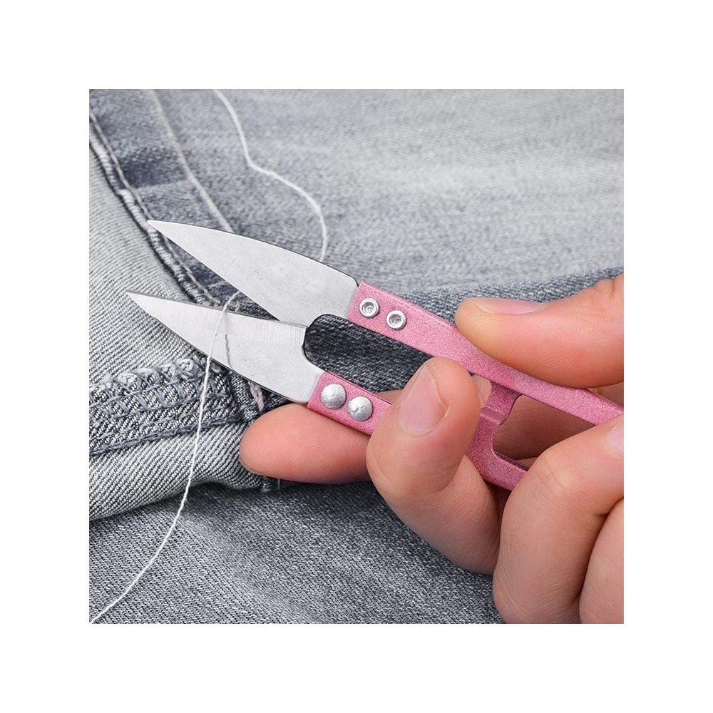 Hand holding pink sewing snip scissors to cut white thread on denim fabric