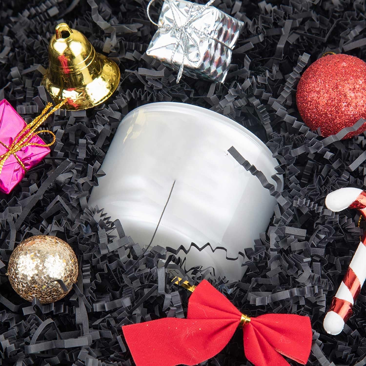 Black crinkle cut paper shred filler with assorted holiday decorations including a bell, ornaments, candy cane, and gift boxes.