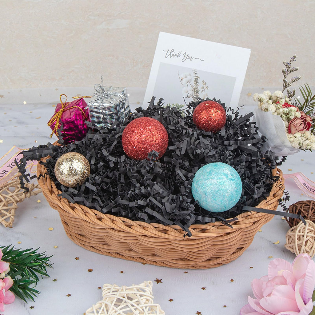 Wicker basket filled with black crinkle paper shred, decorative balls, and small gift boxes, with a 'Thank You' card.
