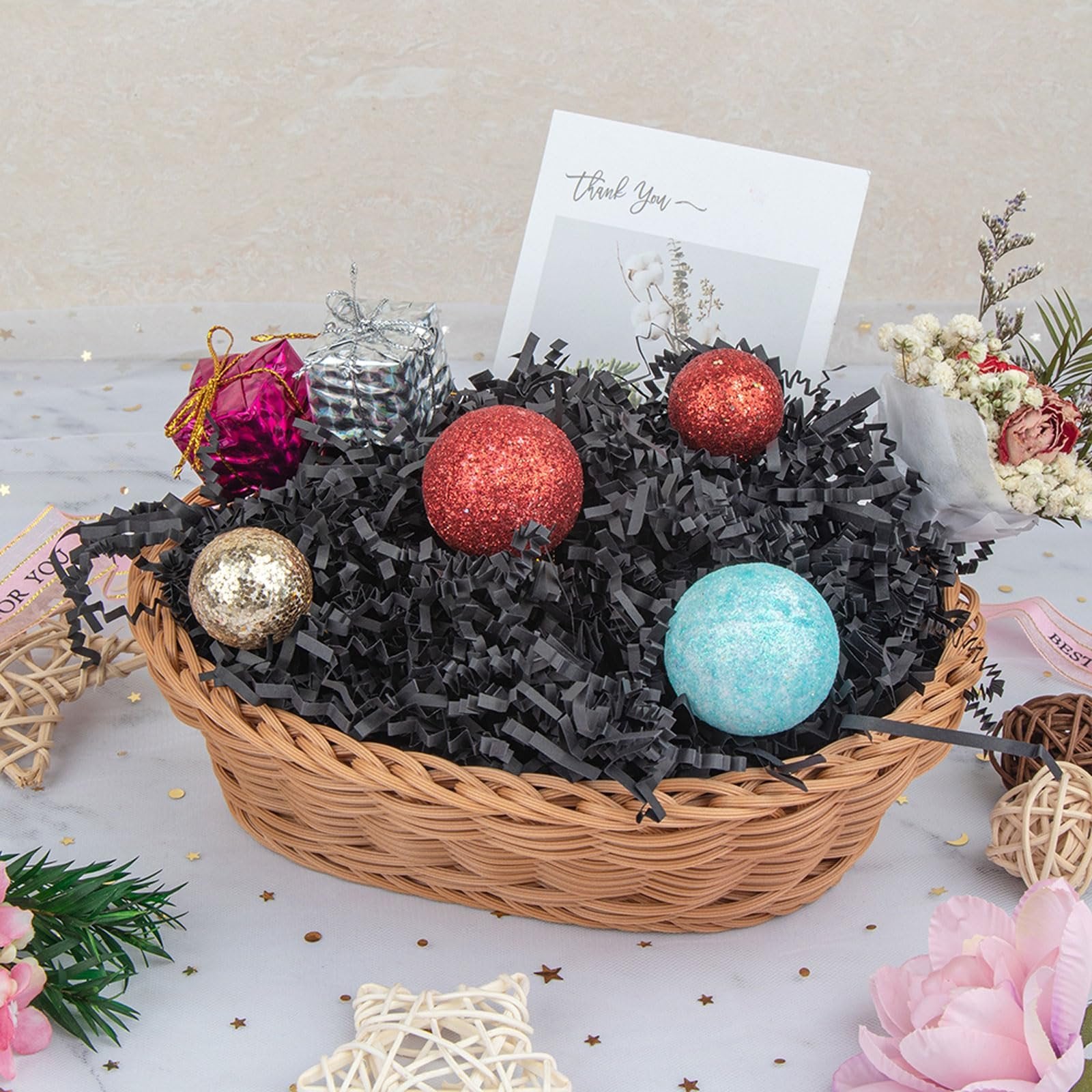 Wicker basket filled with black crinkle paper shred, decorative balls, and small gift boxes, with a 'Thank You' card.