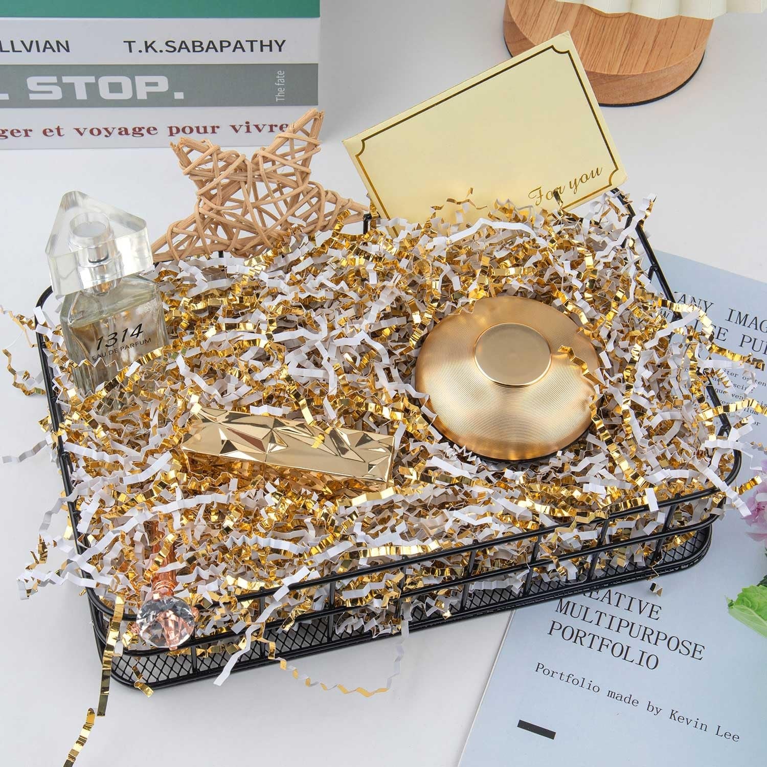 Gift basket filled with white and gold crinkle cut paper shred, containing perfume, a gold compact, and a decorative star.