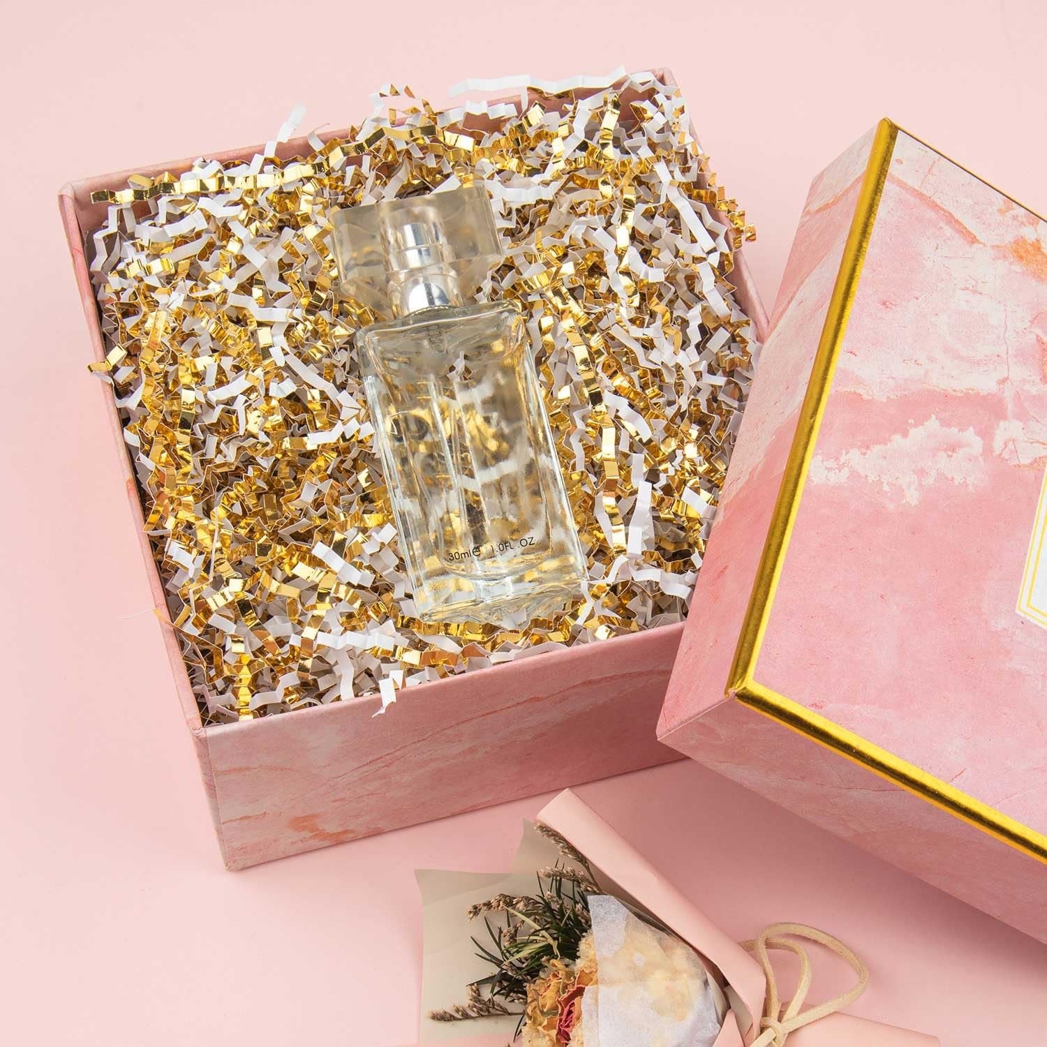 Open gift box filled with white and gold crinkle cut paper shred, with a perfume bottle inside.