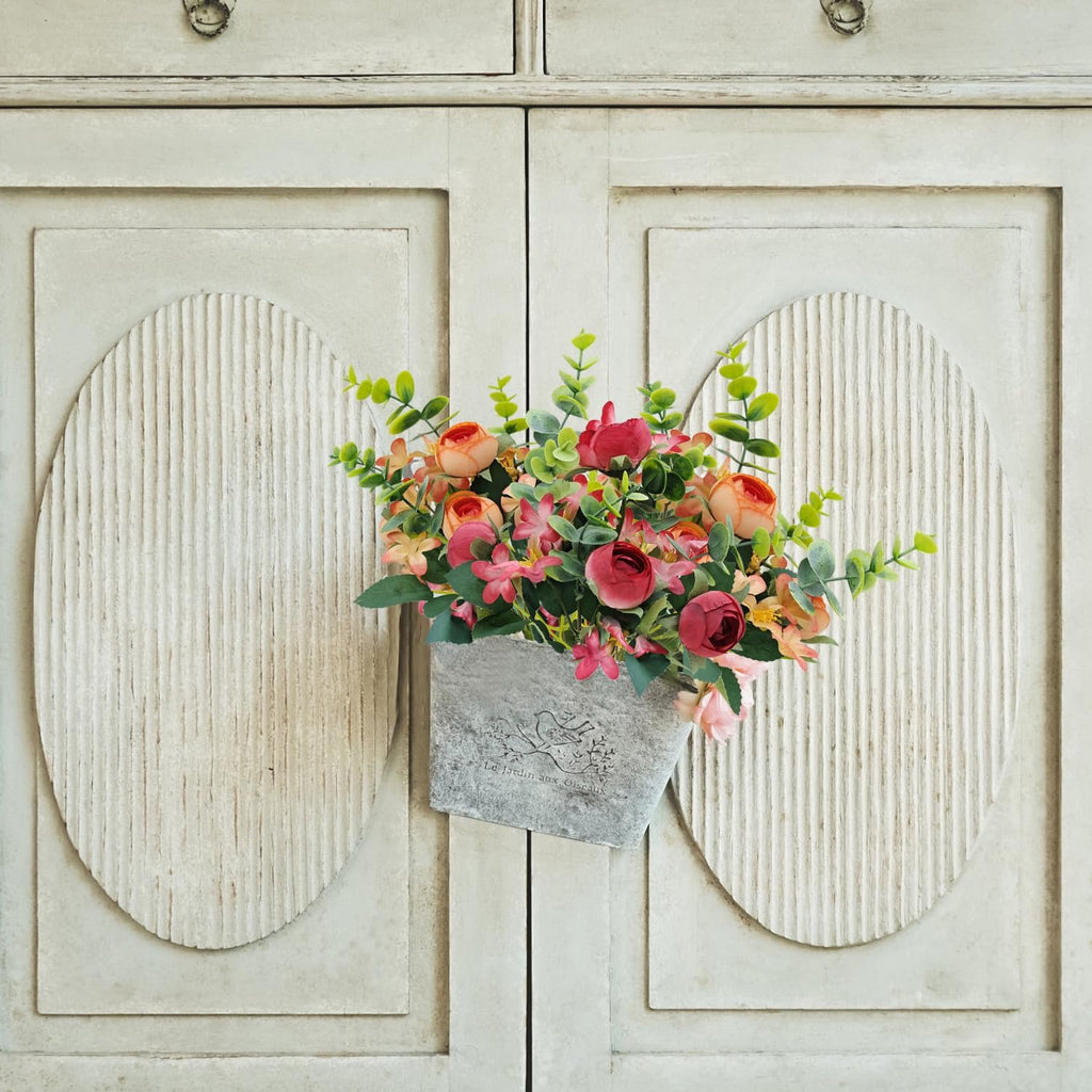 Artificial peony flower bundle with eucalyptus and succulents in a gray planter against a distressed cabinet door