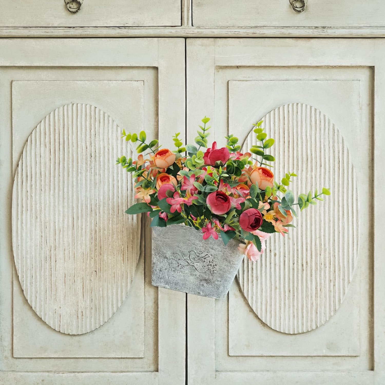 Artificial peony flower bundle with eucalyptus and succulents in a gray planter against a distressed cabinet door