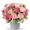 Pink and rose artificial peony bouquet with berries and green leaves in a gray textured vase, front view.