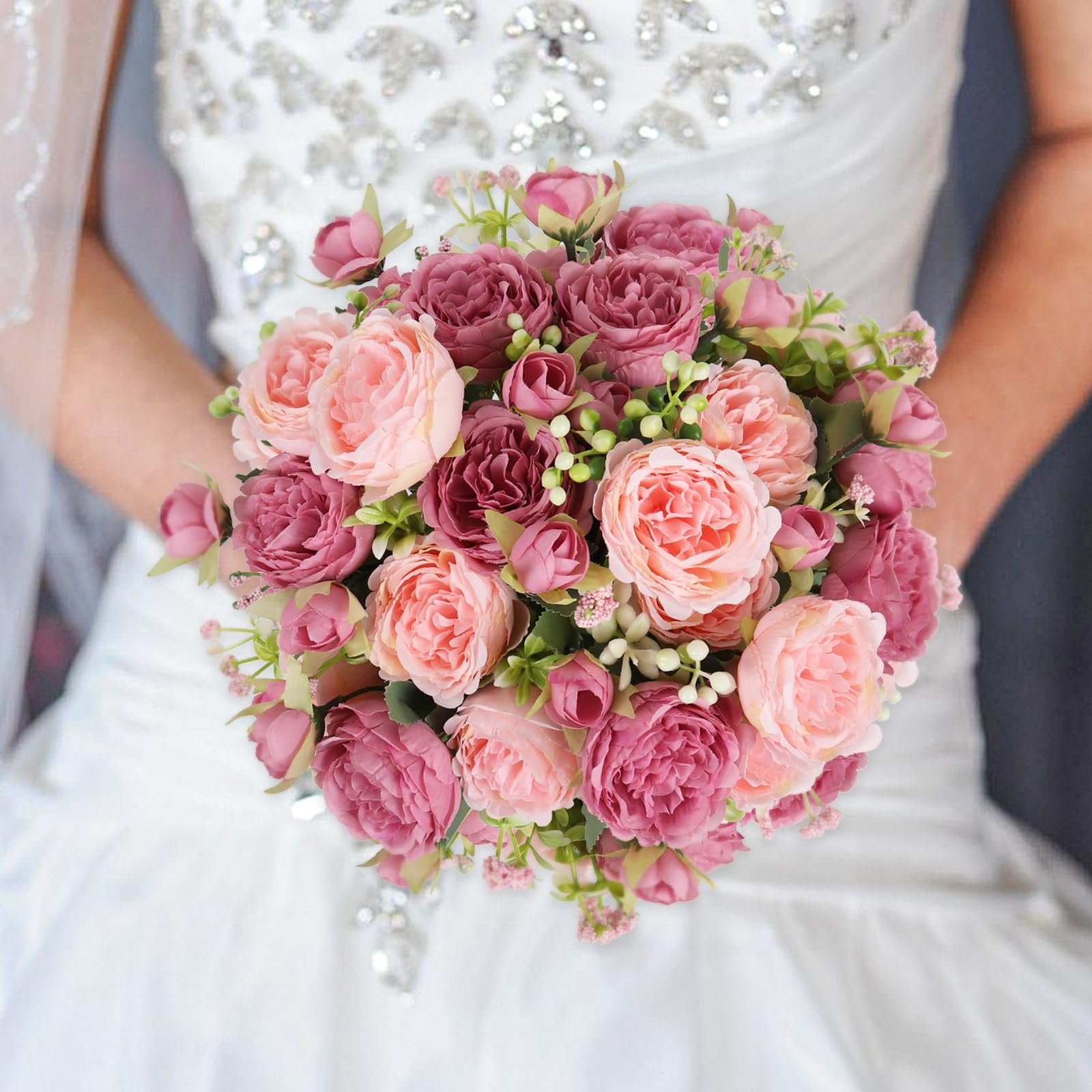 Bride holding a bouquet of pink and deep pink artificial peonies with berries and green leaves