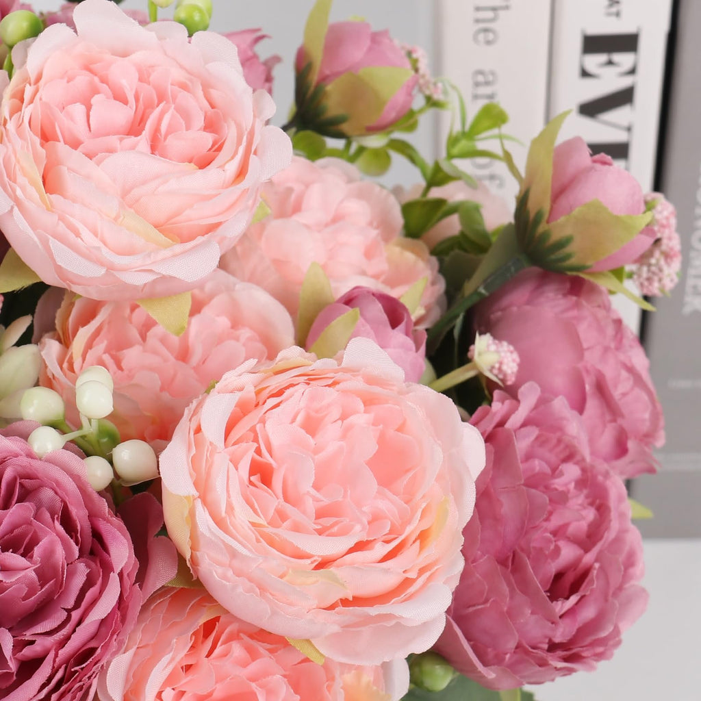 Close-up of a bouquet of artificial pink and purple peonies with green leaves and white berries.