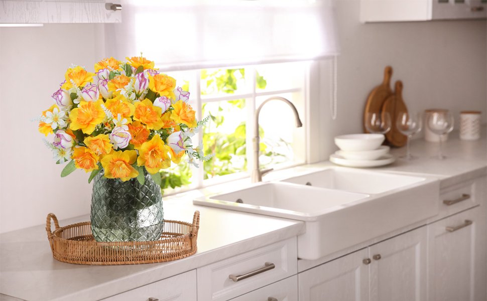 Bouquet of artificial daffodils and tulips in a glass vase on a kitchen counter