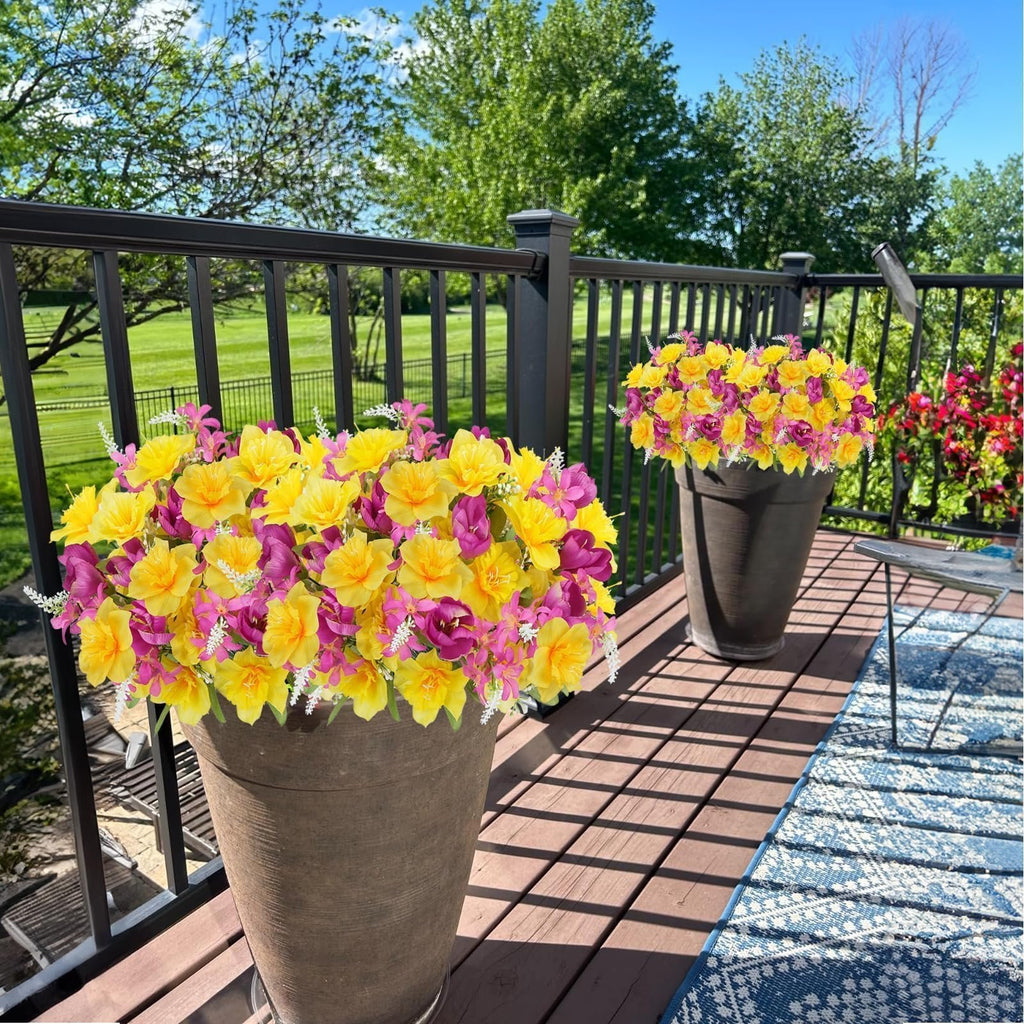 Two large planters filled with yellow and pink artificial flowers on a wooden deck with a railing and green lawn in the background.