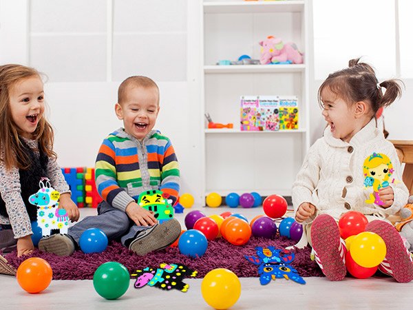 Three laughing children sitting on a rug with colorful balls and foam craft projects