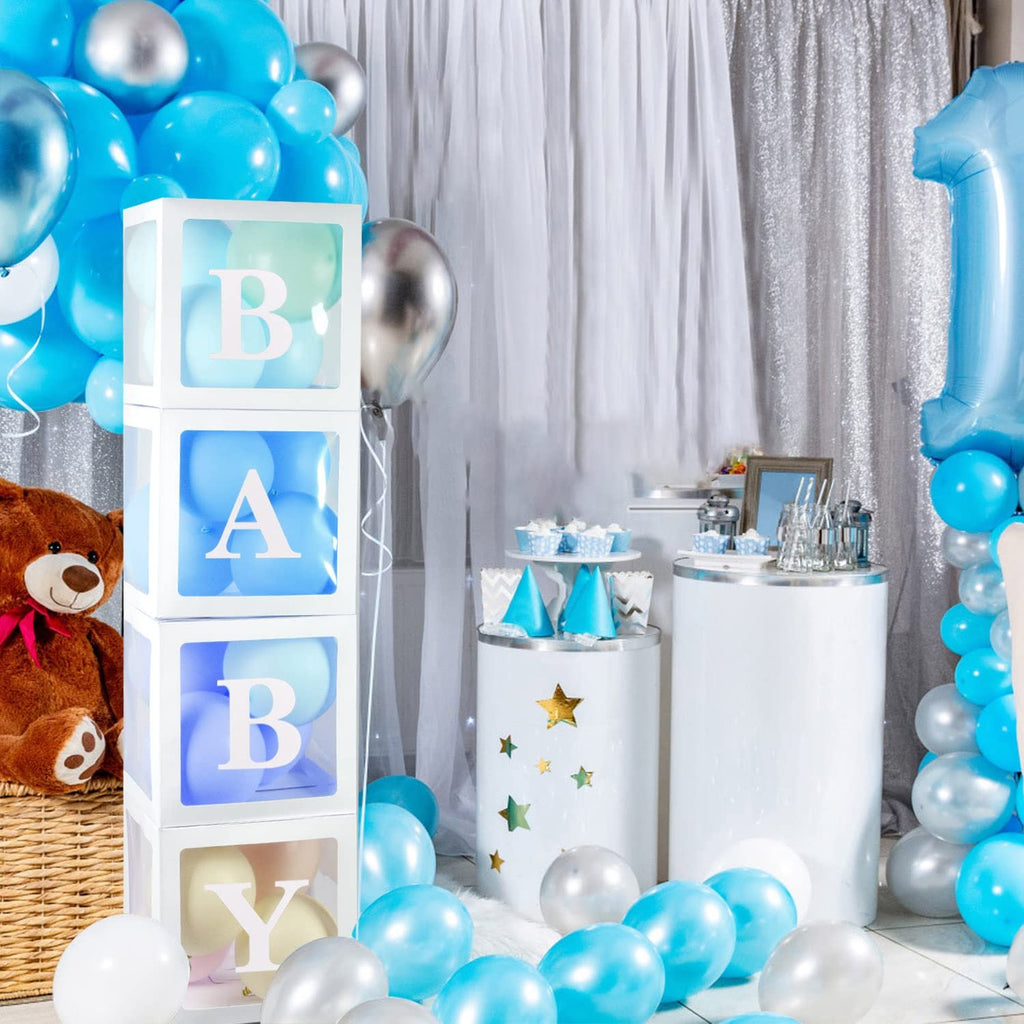 Four clear balloon boxes stacked with BABY letters, surrounded by blue and silver balloons, a teddy bear, and party decor.
