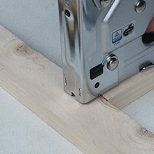 Manual staple gun stapling into wood with a hand holding the handle