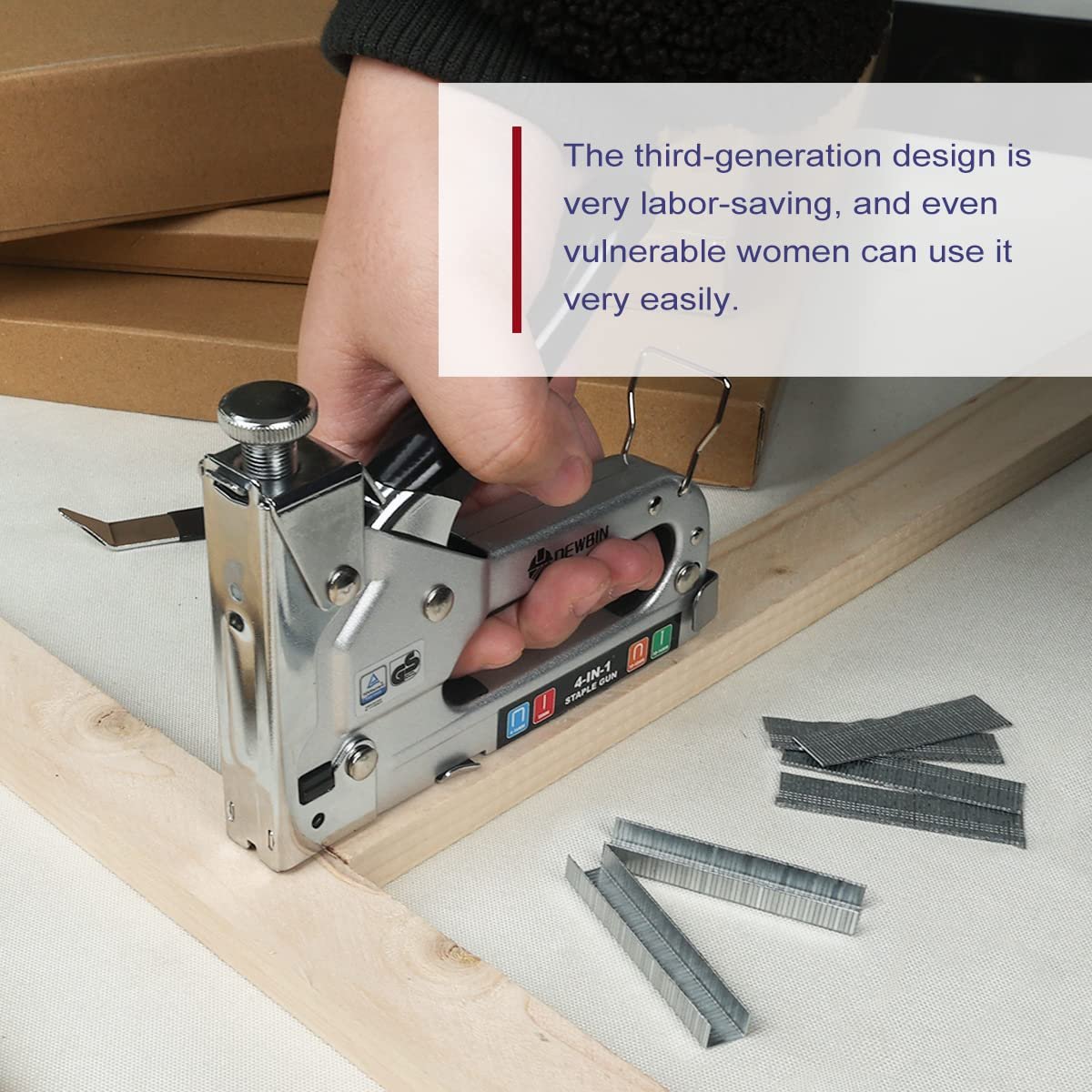 Hand holding a silver 4-in-1 staple gun, using it on a wooden frame with staples nearby.