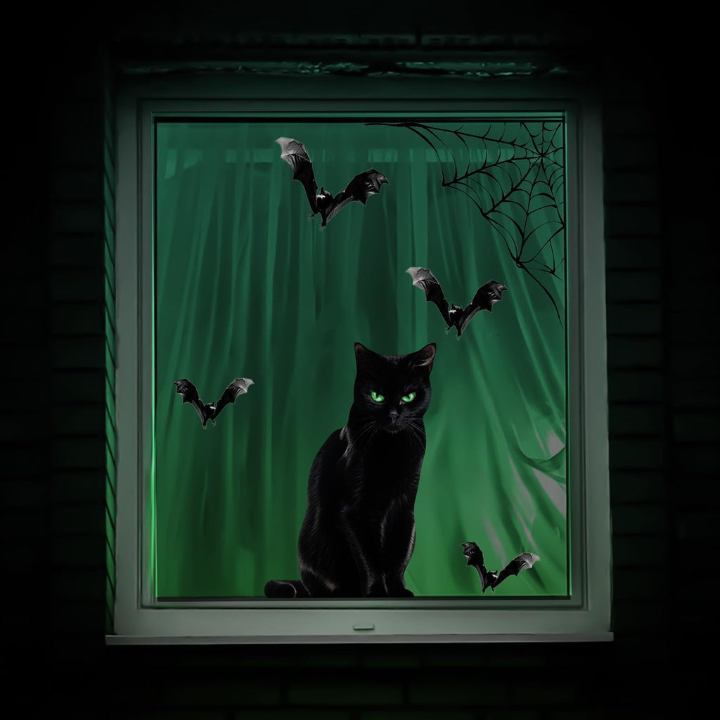 Black cat with green eyes sits on a windowsill with bats and a spiderweb graphic on a green curtained window.
