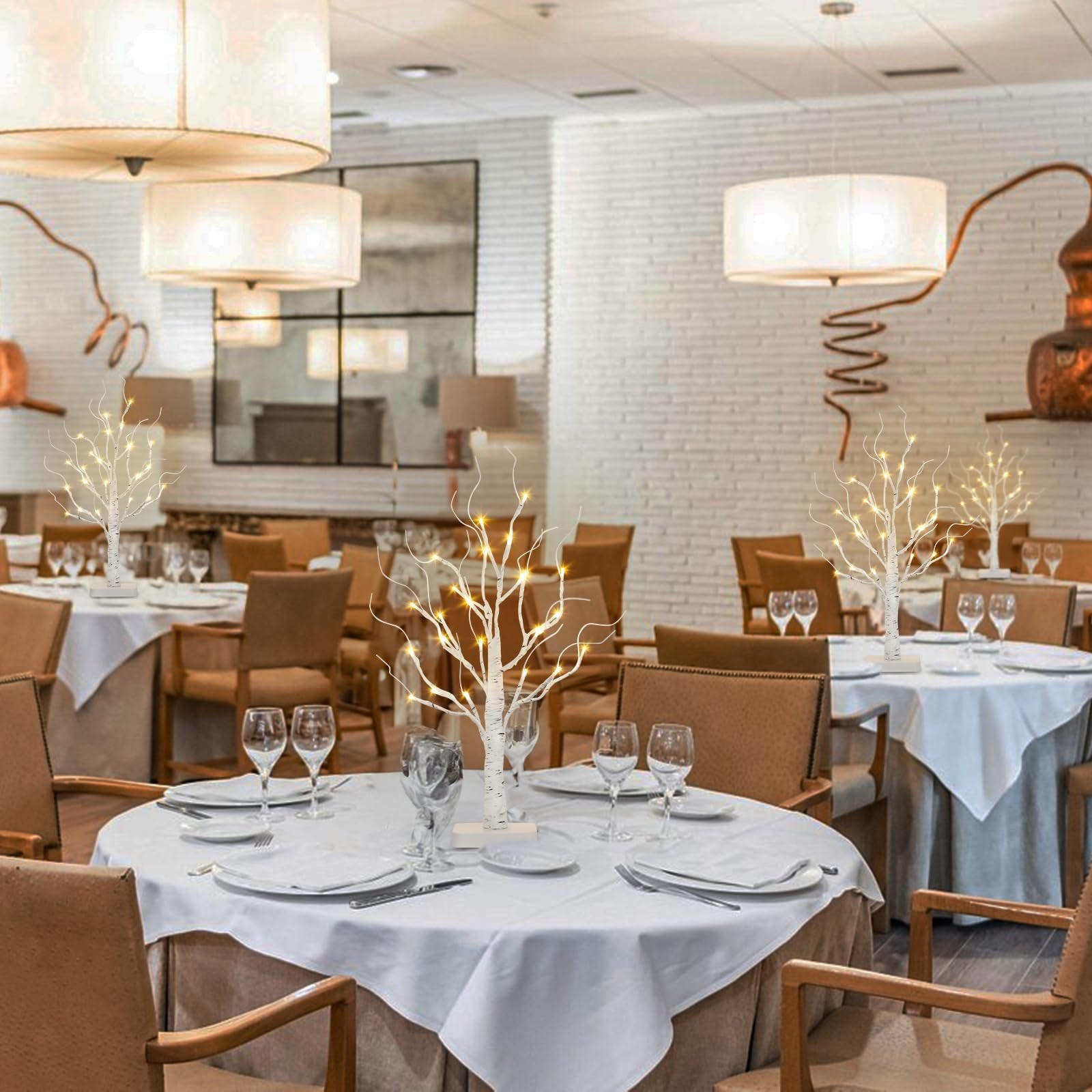 Four lighted white birch tabletop trees with warm white LEDs set on restaurant tables.