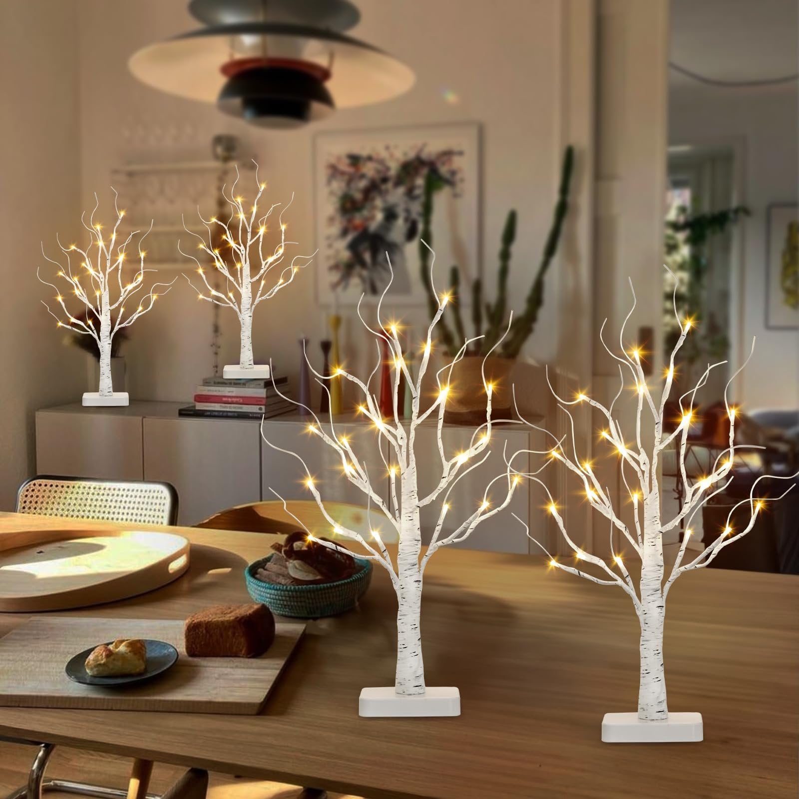 Four lighted white birch tabletop trees with warm white LEDs arranged on a dining table.
