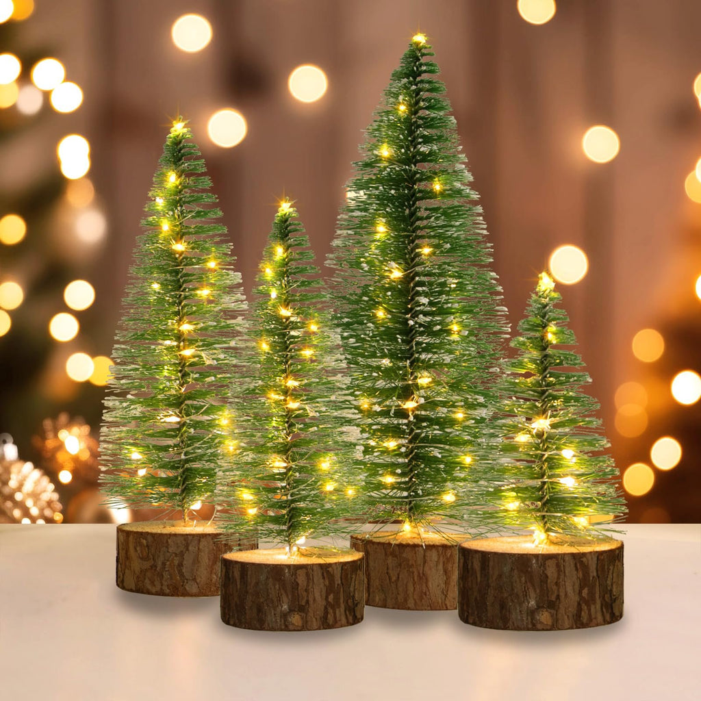 Four mini artificial Christmas trees with warm white LED lights and wooden bases on a table with bokeh background.