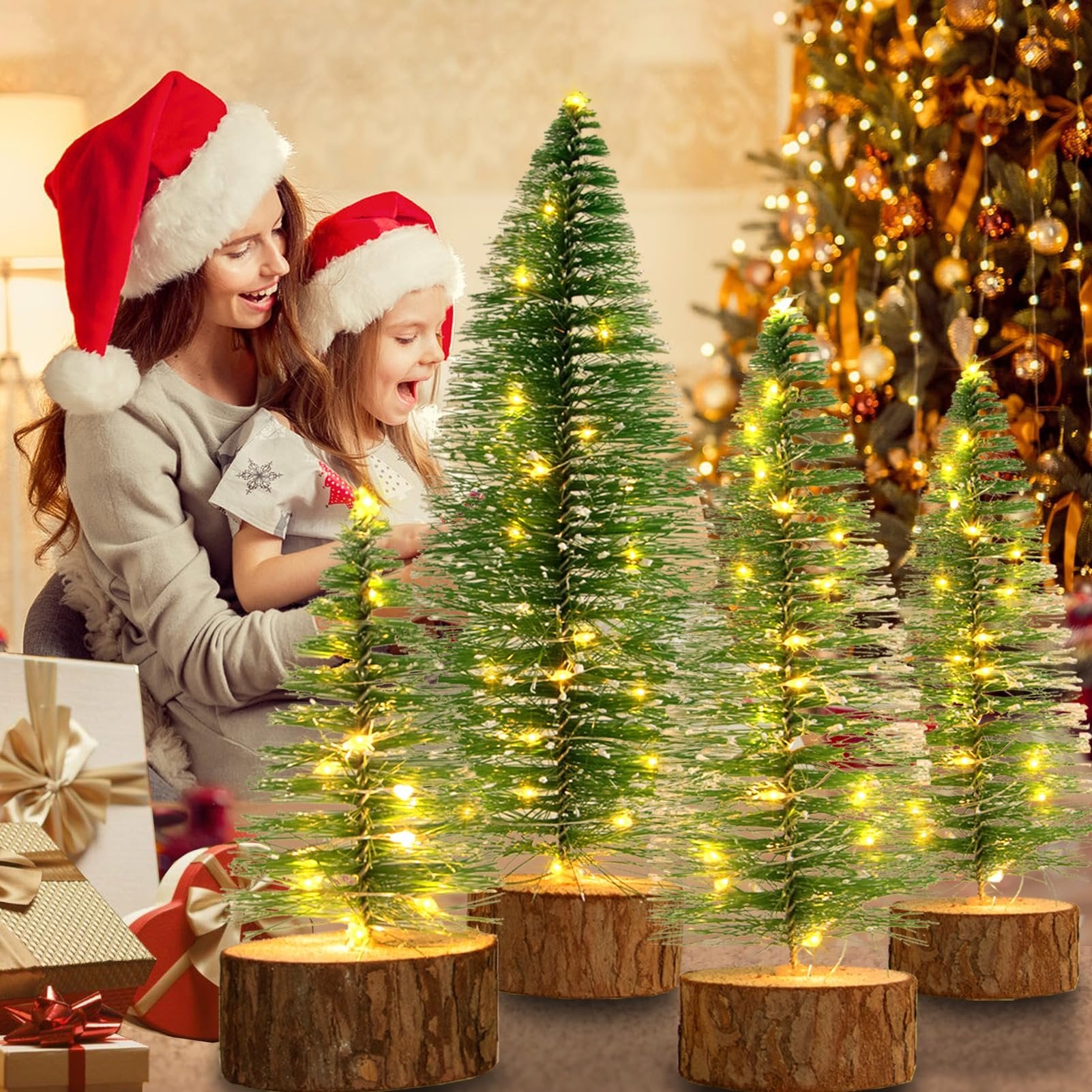 Mother and daughter in Santa hats looking at mini LED Christmas trees with wooden bases, gifts nearby