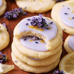 Stack of lavender lemon cookies with purple icing and fresh lavender sprigs, one cookie has a bite taken out.