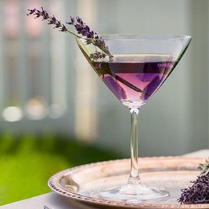 Martini glass with purple liquid and lavender sprig garnish, on a silver tray with dried lavender flowers.