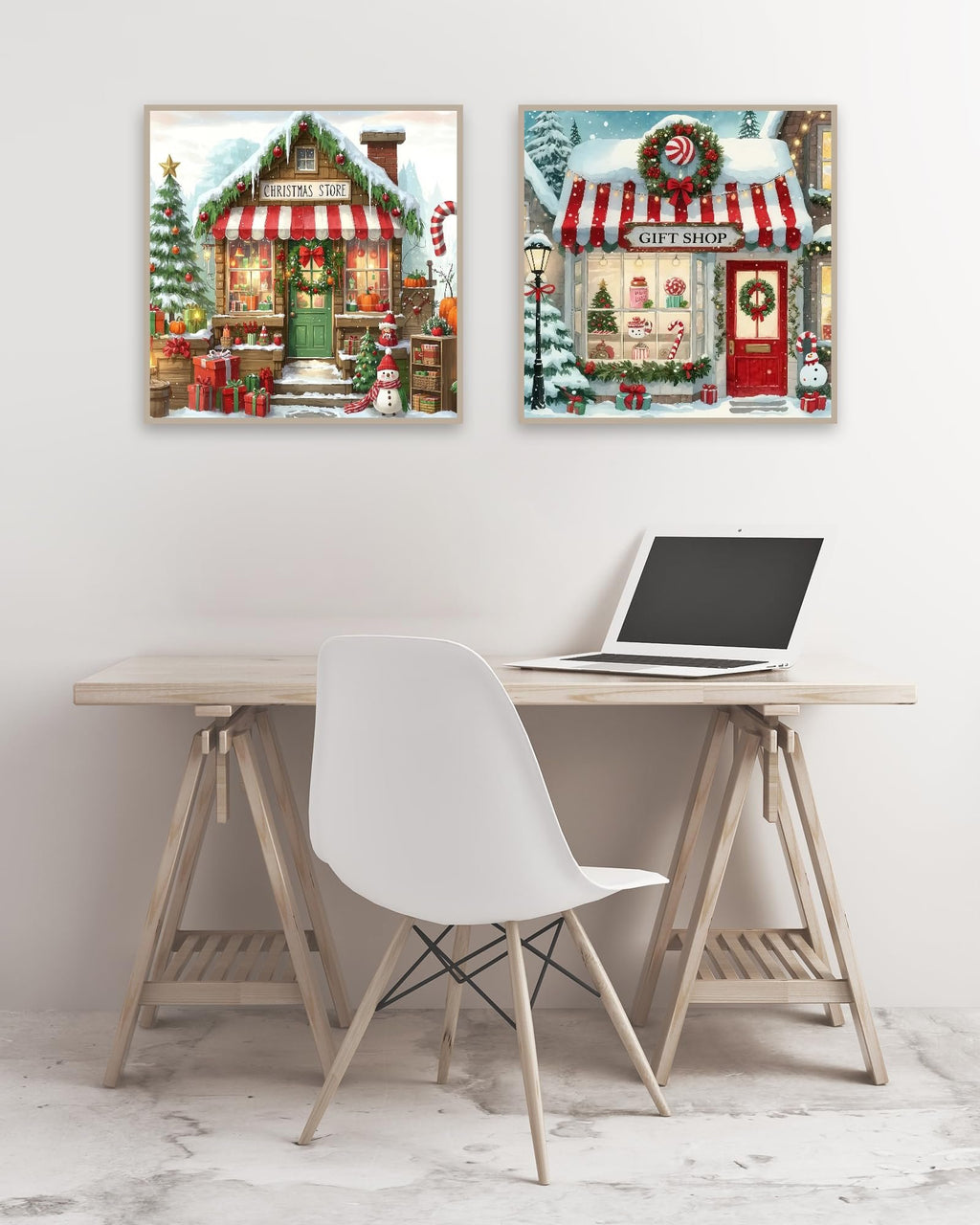 Two framed Christmas store and gift shop scenes displayed on a wall above a desk with a laptop.