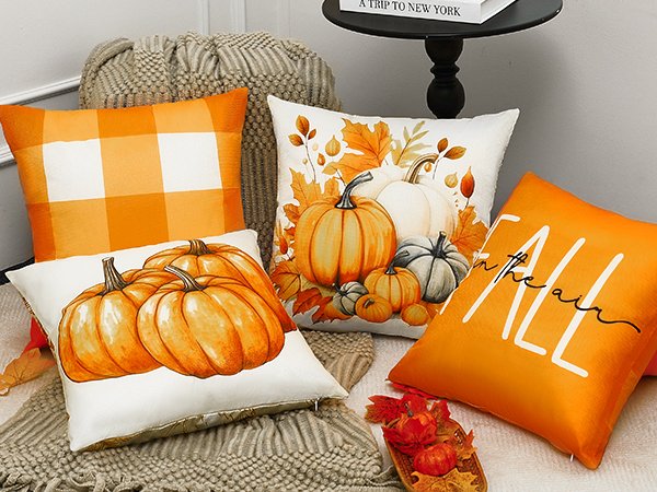 Four fall-themed throw pillow covers arranged on a textured blanket, featuring pumpkins, plaid, and text.