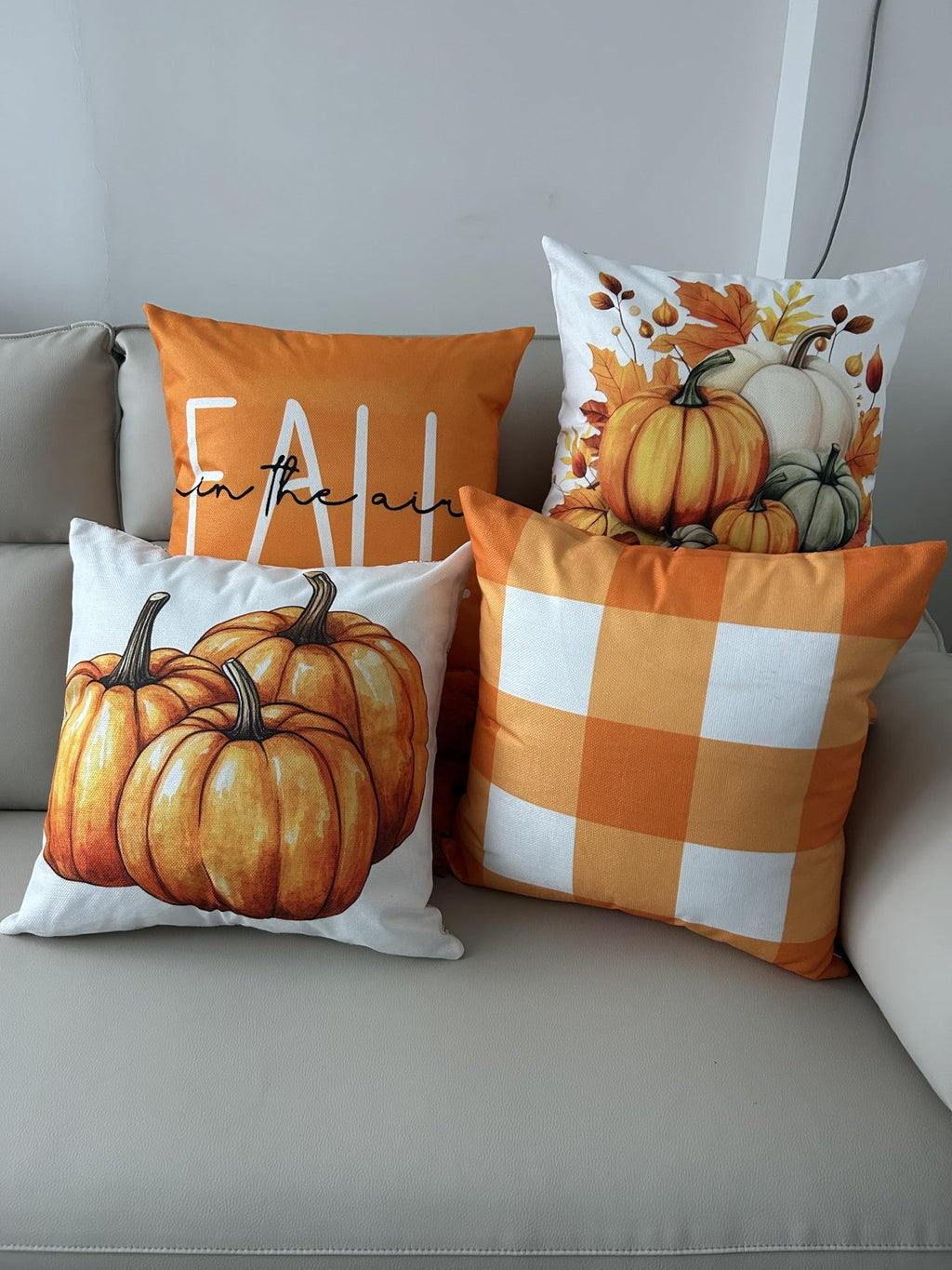 Four fall-themed throw pillow covers with pumpkins and plaid designs arranged on a sofa.