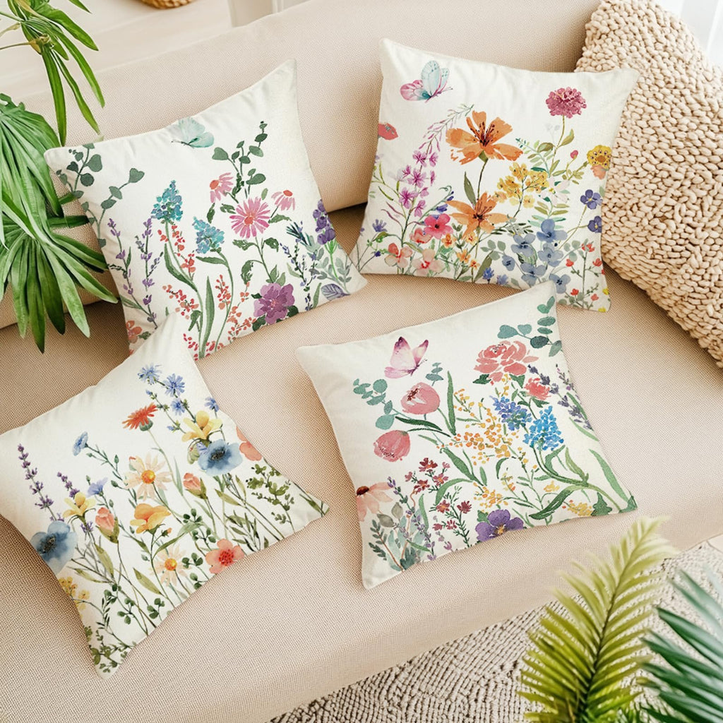 Four square pillow covers with floral and butterfly designs arranged on a sofa.