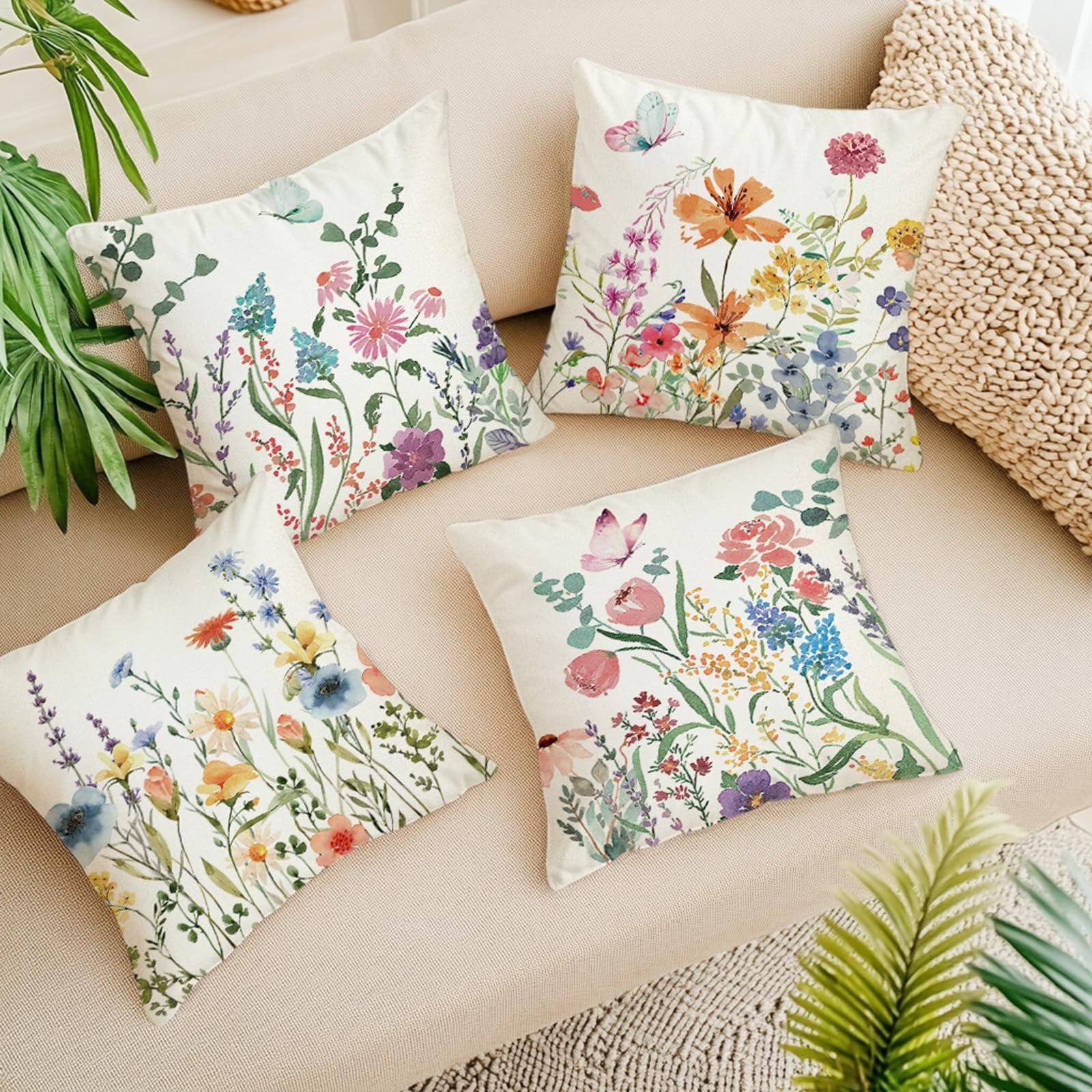 Four square pillow covers with floral and butterfly designs arranged on a sofa.