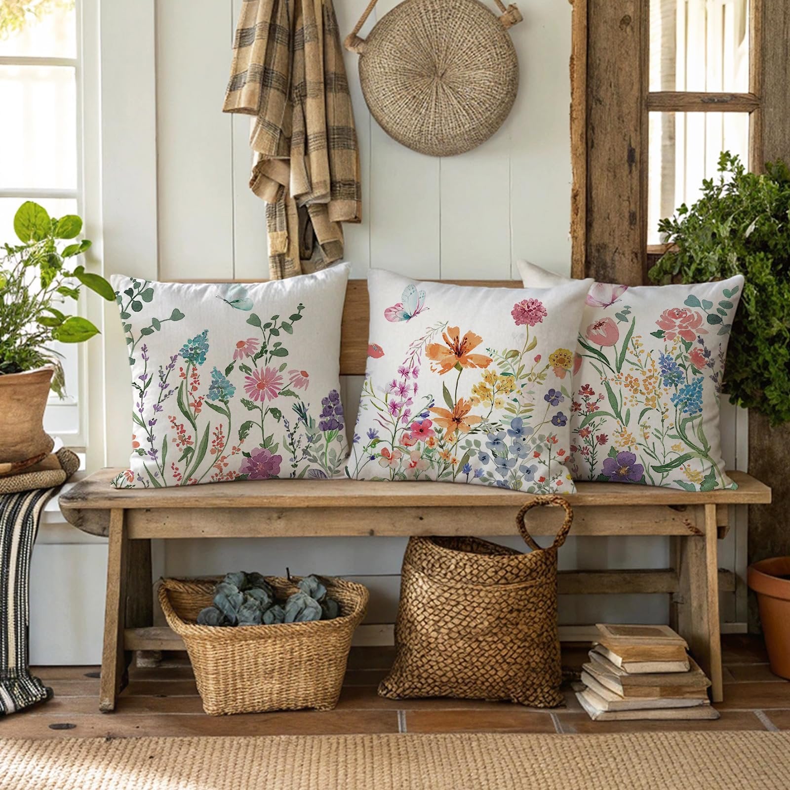 Three floral butterfly print pillow covers displayed on a rustic wooden bench with decorative baskets and plants.