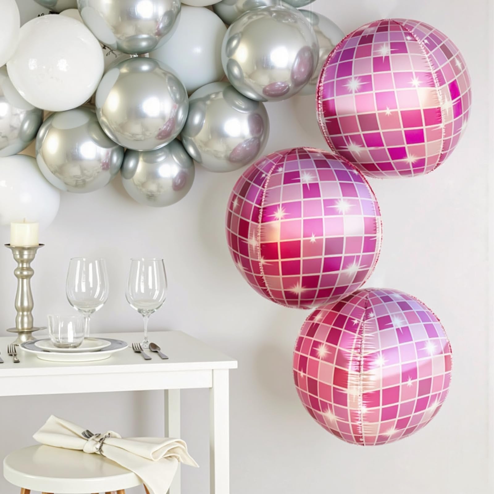 Three pink disco ball balloons and a cluster of silver and white balloons above a table setting.