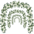 Four cascading artificial rose garlands with white flowers and green leaves arranged in arches on a white background.