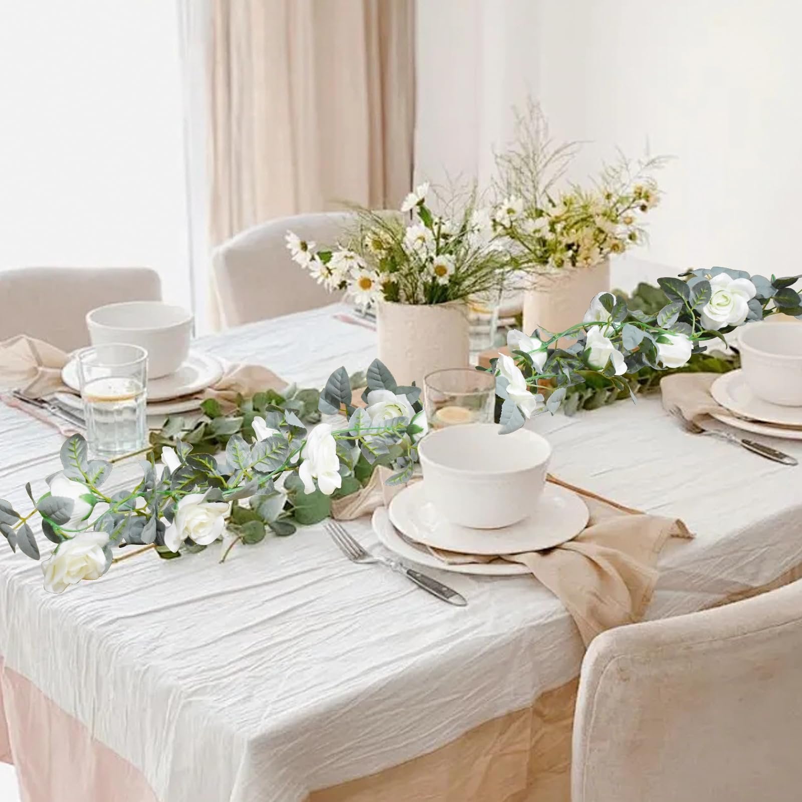 Artificial rose garland with white flowers and green leaves draped across a set dining table