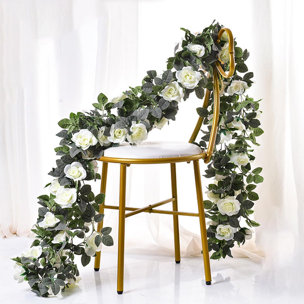 Artificial white rose garland draped over a gold chair with white cushion, against a white backdrop.