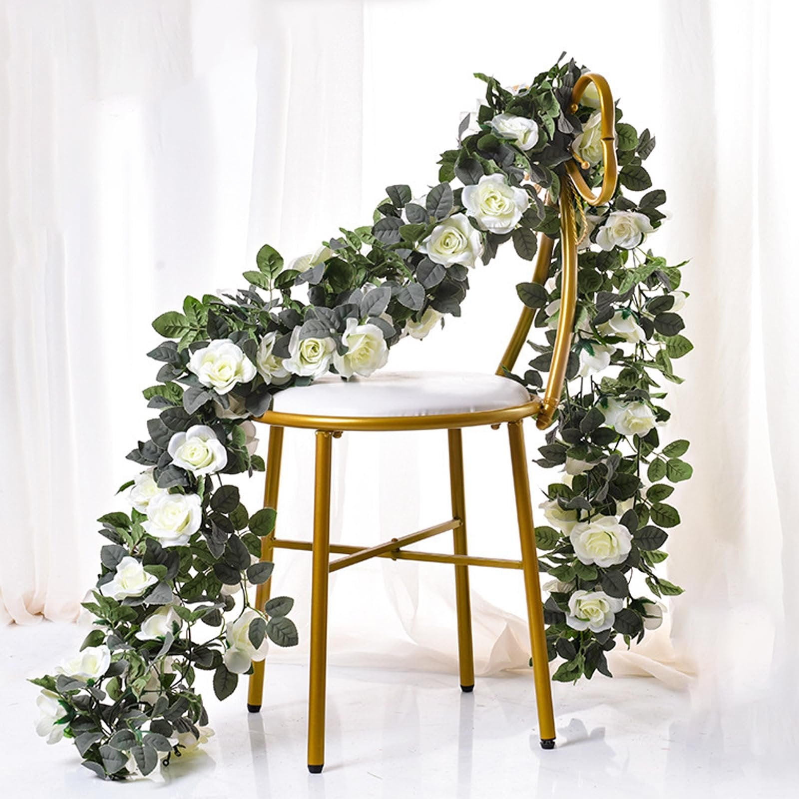 Artificial white rose garland draped over a gold chair with white cushion, against a white backdrop.