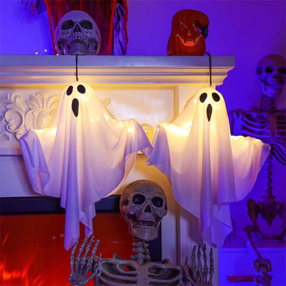 Two lighted white fabric ghost decorations hanging with spooky Halloween skeletons and skulls in the background.