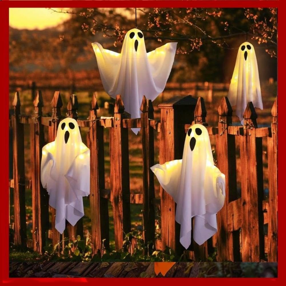 Four lighted white fabric ghost decorations hanging on a wooden fence at dusk